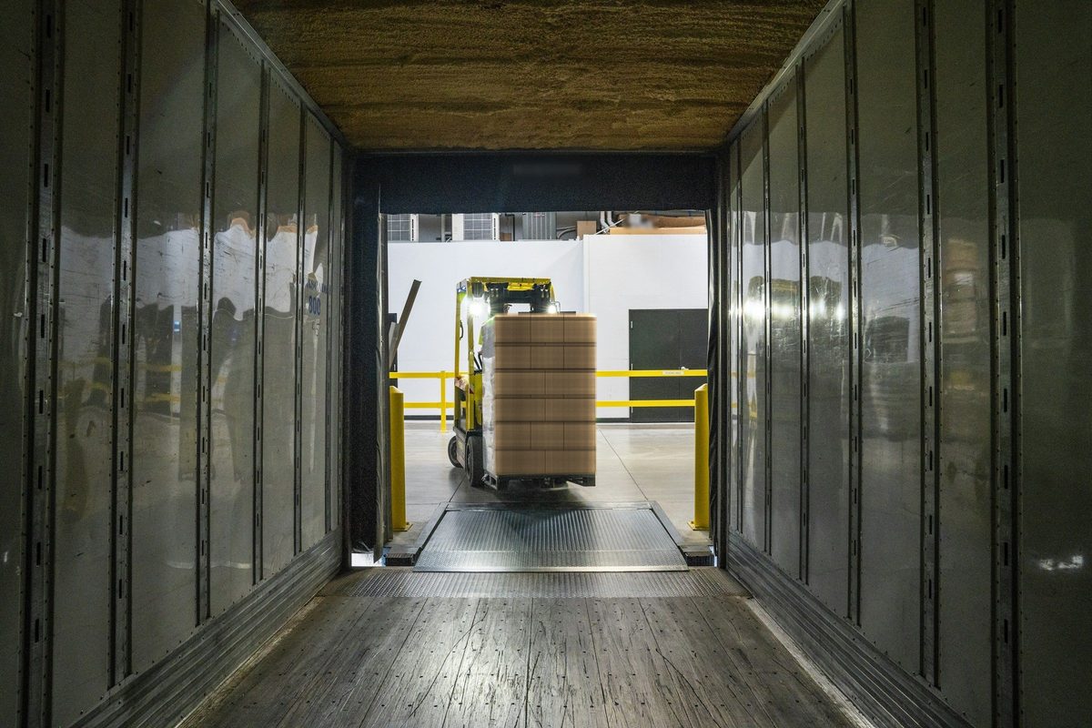A forklift loading a pallet into a truck, seen from inside the trailer.