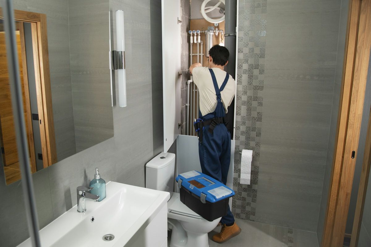 A plumber at work on the pipes of a bathroom job.