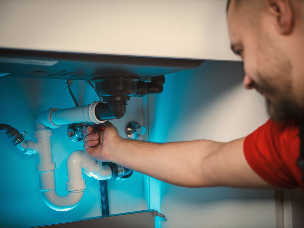 A plumber working on the pipes under a sink.
